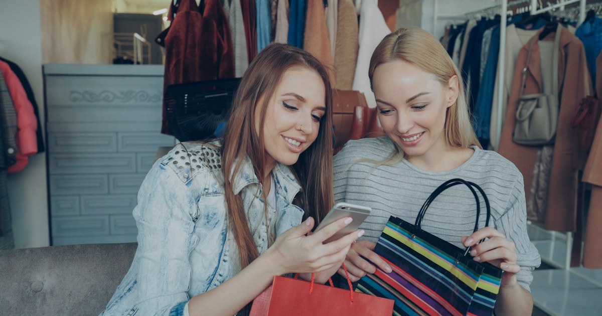 Duas mulheres olhando um celular dentro de uma loja de roupas