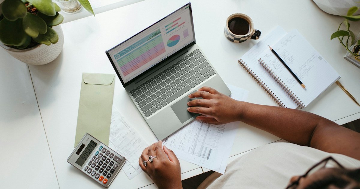Mesa de trabalho com notebook mostrando gráficos, calculadora e anotações