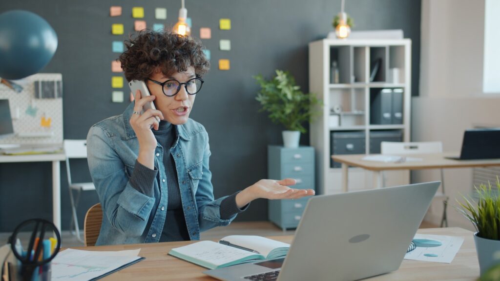 A business owner at a desk talking on the phone while working at a laptop