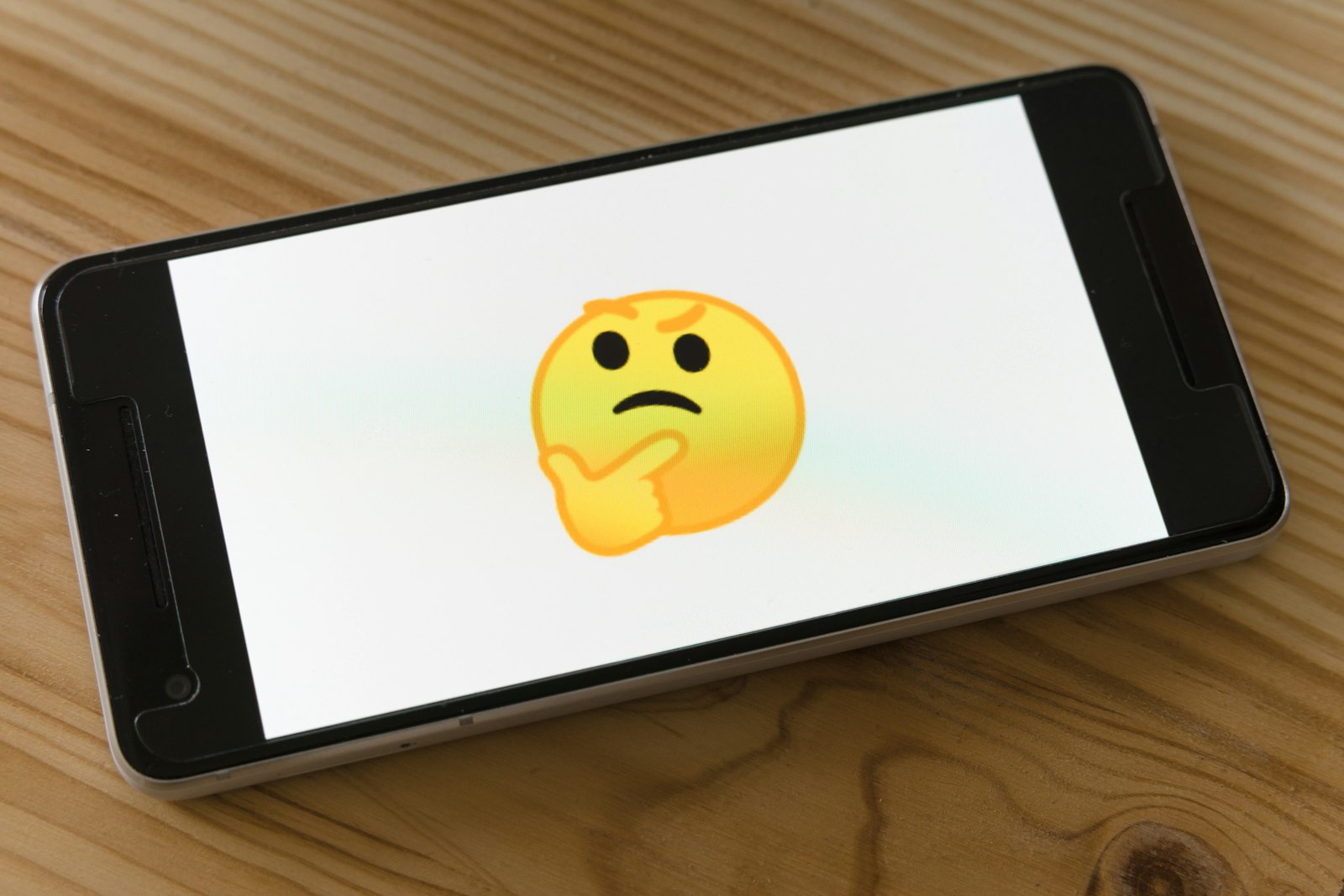 A smartphone on a wooden table showing a thinking-face emoji